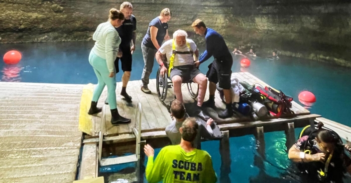 People helping scubility diver into the water
